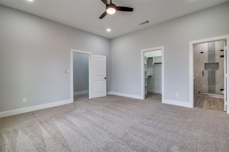 Unfurnished bedroom featuring ceiling fan, a spacious closet, ensuite bathroom, and light carpet