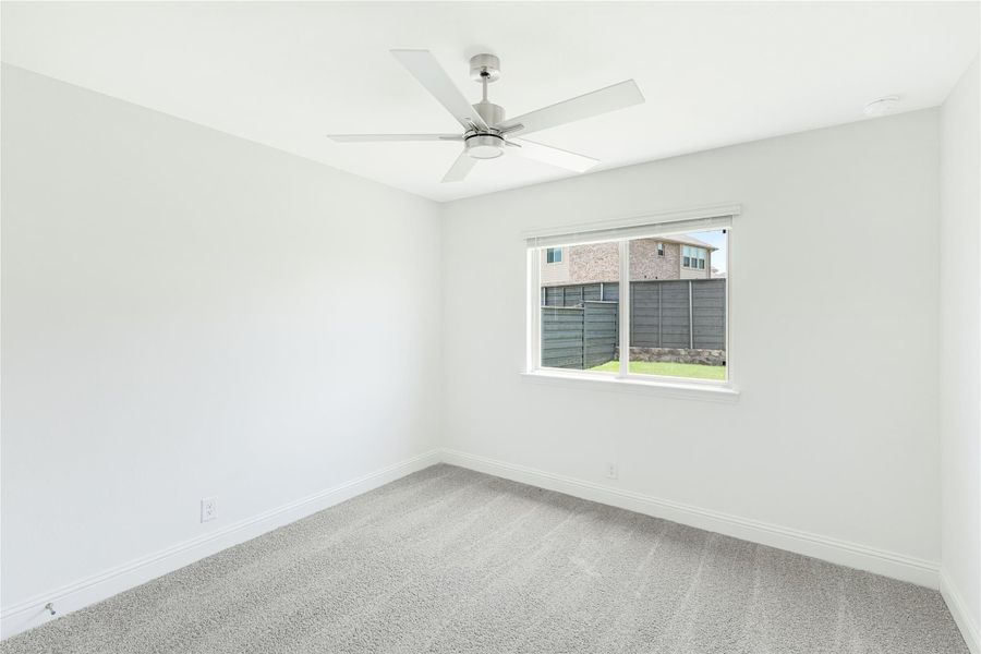 Empty bedroom with gray carpet, ceiling fan, and single window with backyard view Empty bedroom with gray carpet, ceiling fan, and single window with backyard view