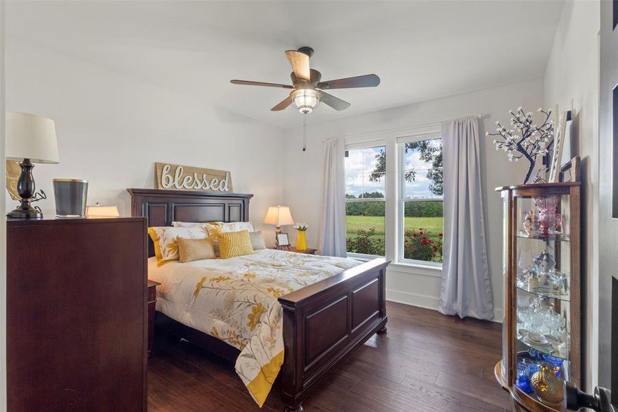 Comfortable second bedroom featuring warm hardwood flooring, abundant natural light, and peaceful acreage views—offering an inviting retreat with classic country elegance and refined simplicity.
