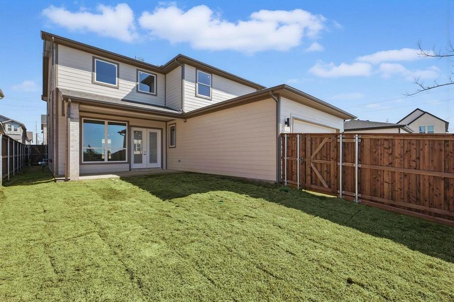 Back of property with a lawn, an attached garage, fence, and a gate