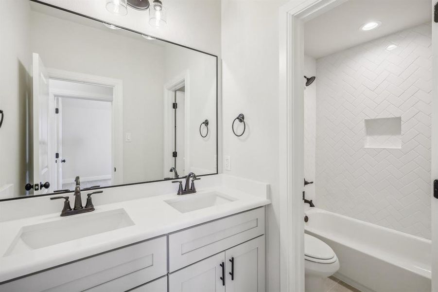 Full bathroom with tile patterned flooring, toilet, double sink vanity, and tiled shower / bath combo