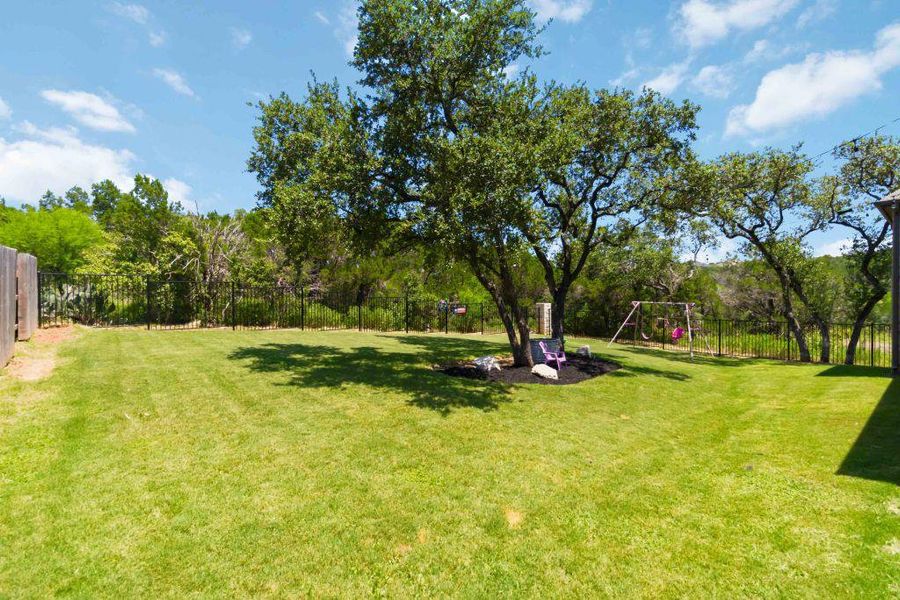 A verdant backyard offers ample space for play and relaxation, bordered by a secure fence and mature trees.