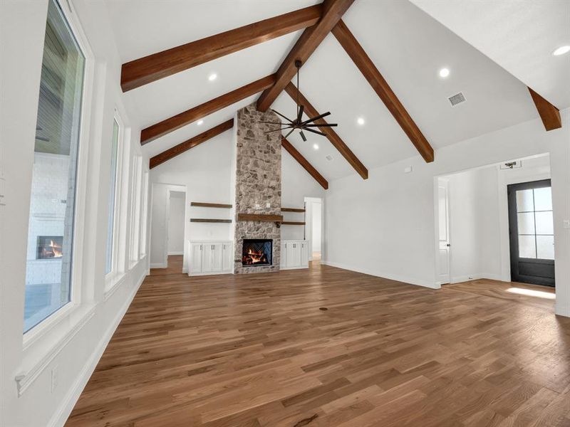 Unfurnished living room with high vaulted ceiling, a stone fireplace, hardwood / wood-style flooring, ceiling fan, and beamed ceiling