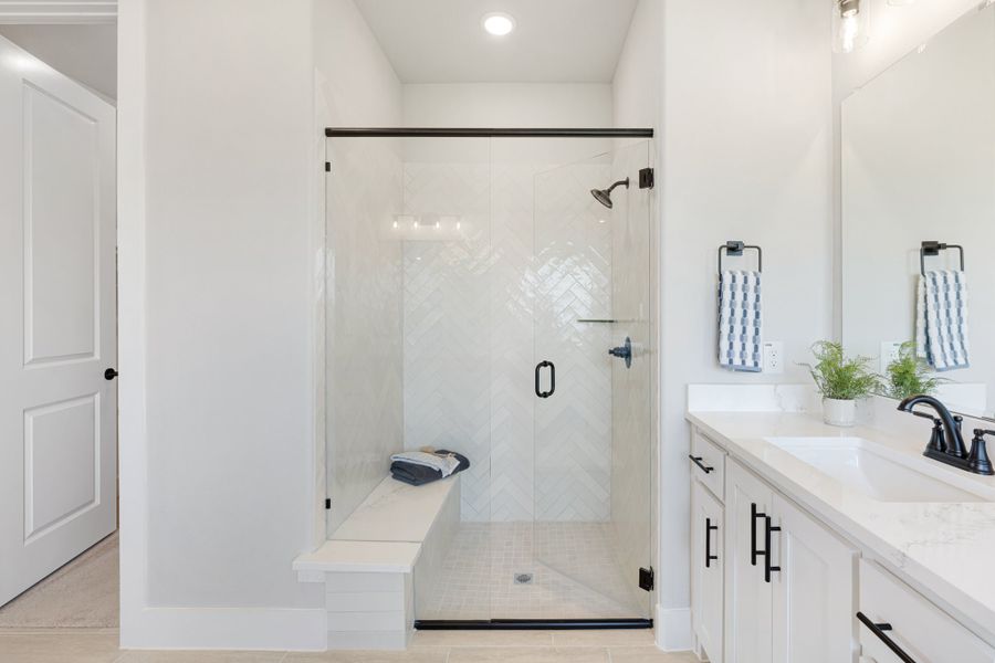 Bathroom with glass walk-in shower featuring herringbone tile, built-in bench, and white vanity with dark hardware