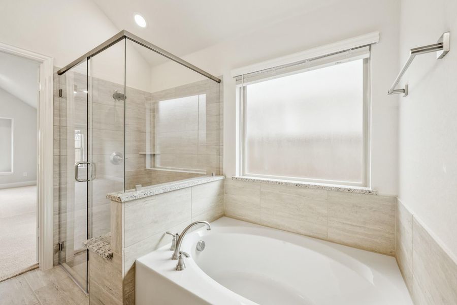 Master bathroom with soaking tub, glass-enclosed shower, and tile surround next to a frosted window Master bathroom with soaking tub, glass-enclosed shower, and tile surround next to a frosted window