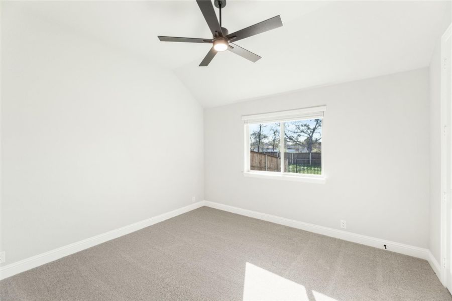 Empty bedroom with vaulted ceiling, ceiling fan, carpet flooring, and single window overlooking backyard fence Empty bedroom with vaulted ceiling, ceiling fan, carpet flooring, and single window overlooking backyard fence