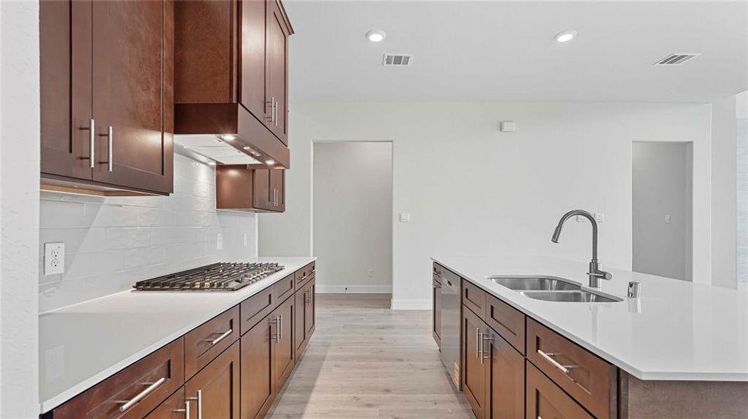 Modern kitchen featuring dark wood cabinetry, white countertops, a gas cooktop, and an island with a double basin sink