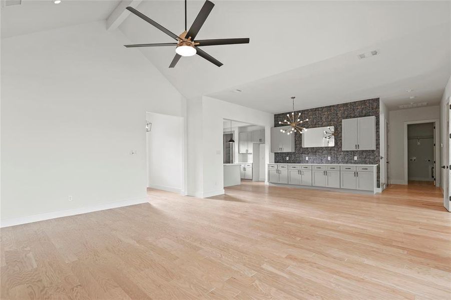 Unfurnished living room featuring high vaulted ceiling, a chandelier, beam ceiling, ceiling fan, and light wood-style floors Unfurnished living room featuring high vaulted ceiling, a chandelier, beam ceiling, ceiling fan, and light wood-style floors