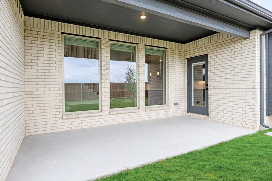 Covered back patio with concrete floor, brick exterior, large windows, and glass back door overlooking fenced yard