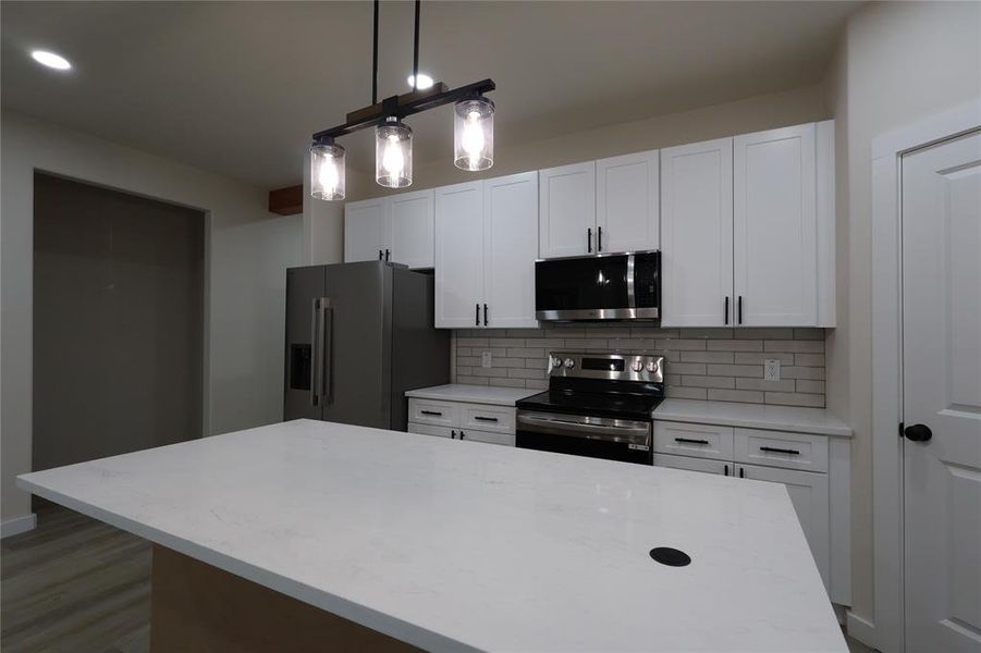 Kitchen featuring stainless steel appliances, decorative backsplash, a kitchen island, white cabinetry, and decorative light fixtures