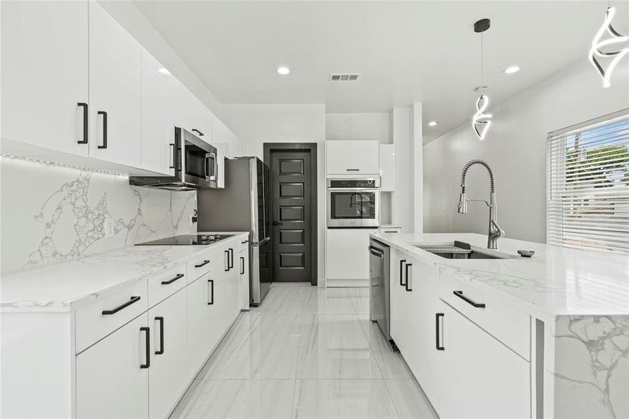 Kitchen featuring appliances with stainless steel finishes, modern cabinets, light marble finish floors, tasteful backsplash, and white cabinetry Kitchen featuring appliances with stainless steel finishes, modern cabinets, light marble finish floors, tasteful backsplash, and white cabinetry