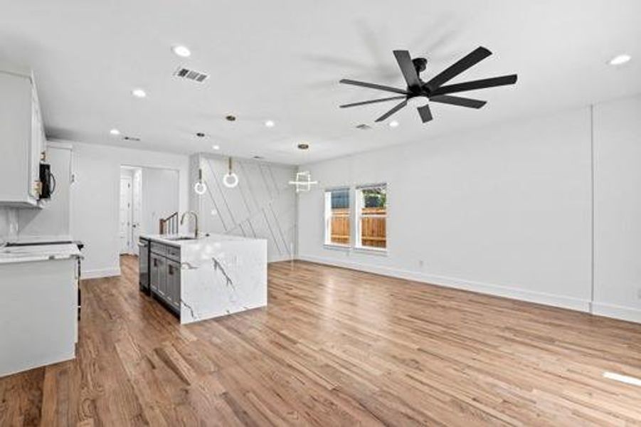 Kitchen with ceiling fan, pendant lighting, light hardwood / wood-style floors, white cabinetry, and an island with sink