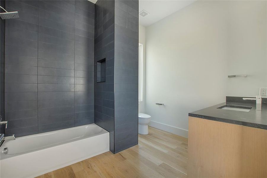 Full bathroom with hardwood / wood-style floors, toilet, vanity, and tiled shower / bath