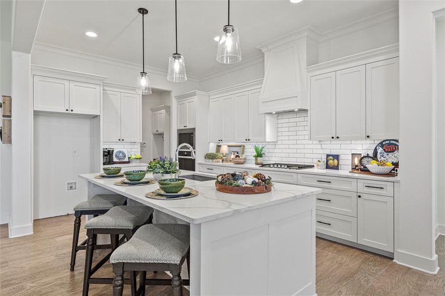 Kitchen featuring white cabinetry, light hardwood / wood-style flooring, a kitchen island with sink, decorative backsplash, and sink