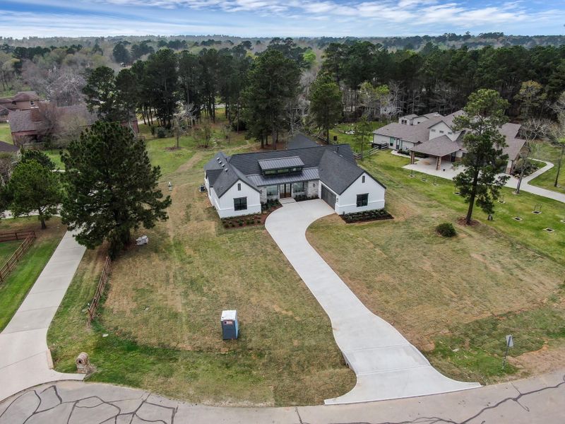 Aerial view showcasing the custom modern farmhouse situated on a spacious 1.04-acre homesite with a sweeping driveway and mature trees surrounding the property.