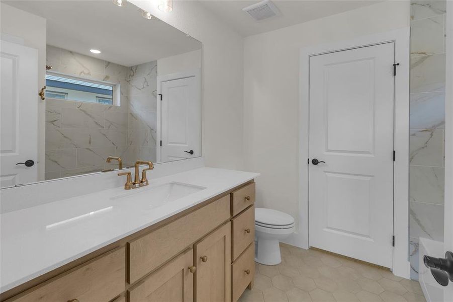 Bathroom featuring a light wood-finish vanity with a white countertop and brass-finish faucet