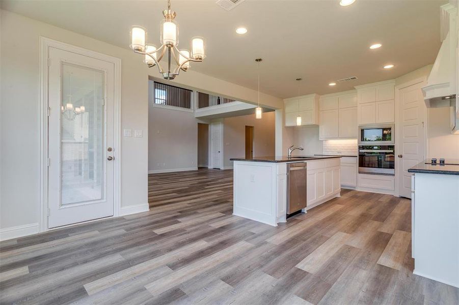 Kitchen with appliances with stainless steel finishes, hanging light fixtures, decorative backsplash, and light hardwood / wood-style floors