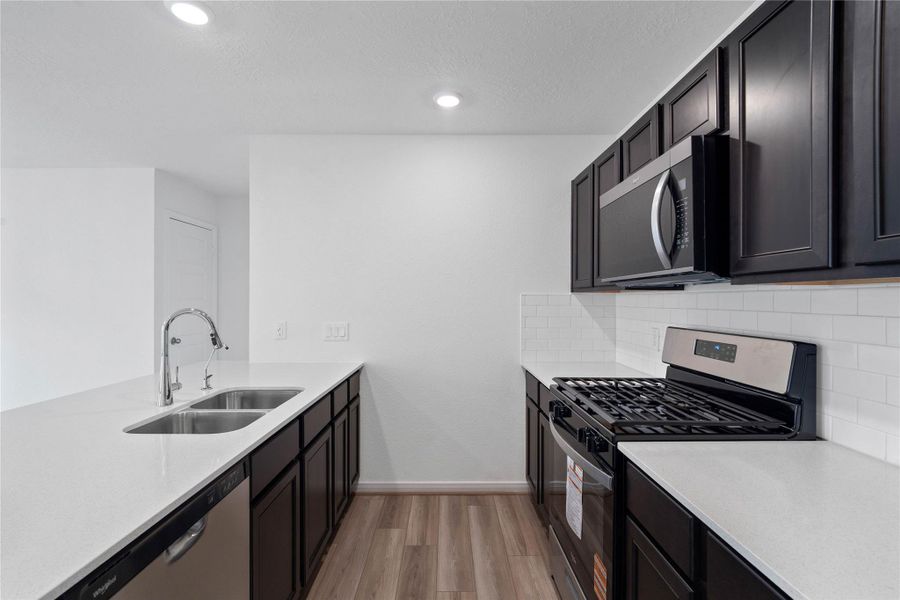 The kitchen features high ceilings, recessed lighting, gorgeous Woodmont cabinetry, stainless steel Whirlpool appliances, quartz countertops, a modern backplash, and a pantry - all overlooking the Great Room.