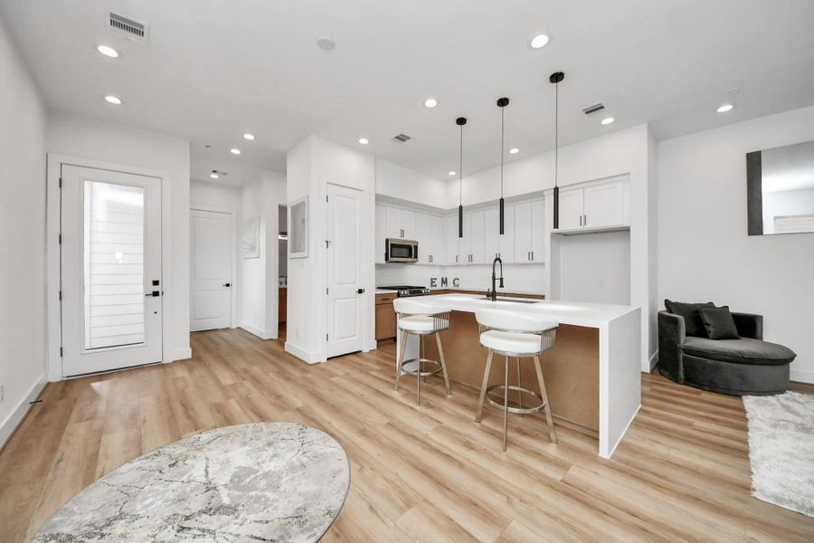 Discover the first floor's seamless blend of elegance and functionality, featuring an open-concept kitchen with sleek white cabinetry, modern lighting, and inviting wood floors that flow into a cozy living space perfect for entertaining or relaxing.