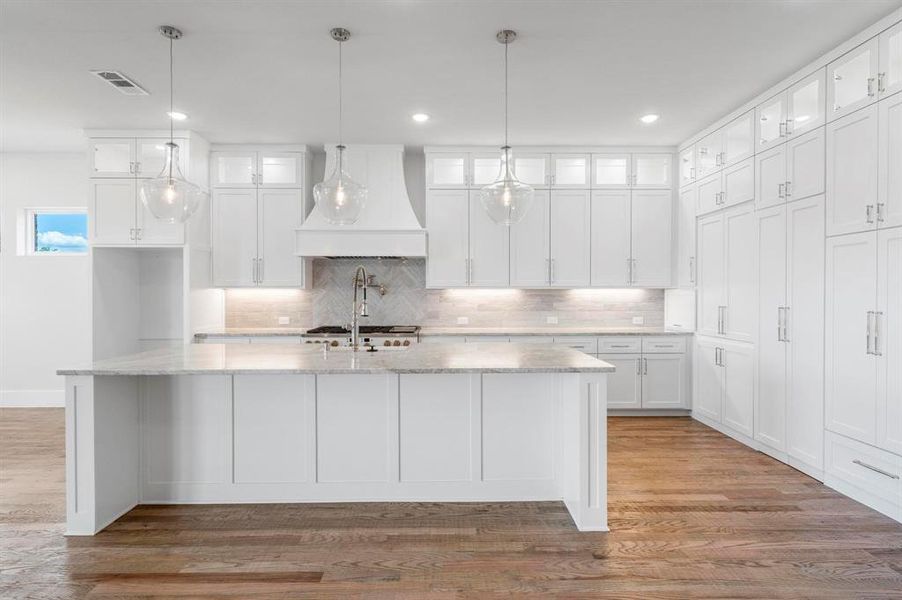 Kitchen featuring premium range hood, white cabinets, light stone counters, an island with sink, and dark hardwood / wood-style flooring