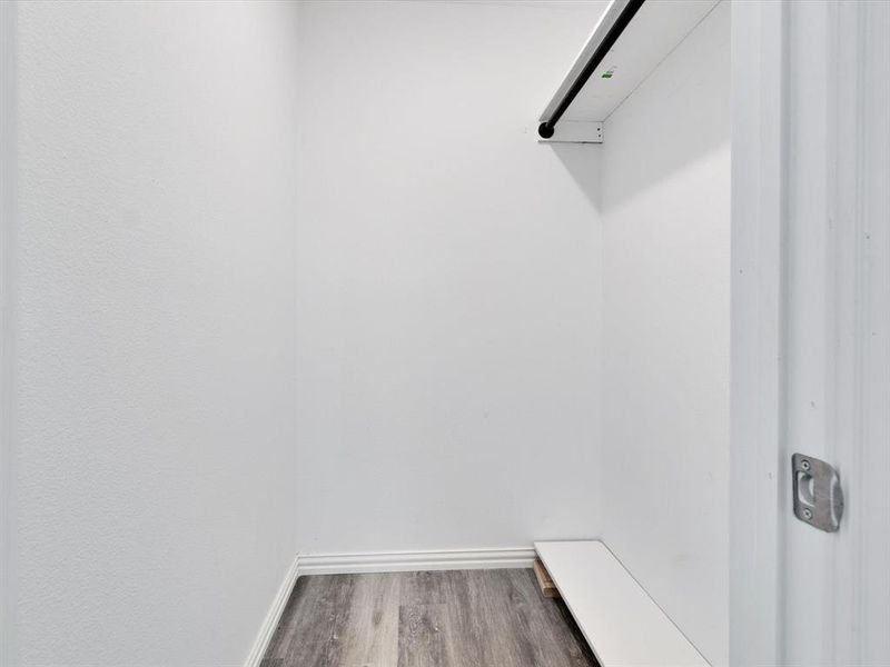Reach-in closet featuring a hanging rod, integrated shelving, wood-finish flooring, and crisp white walls
