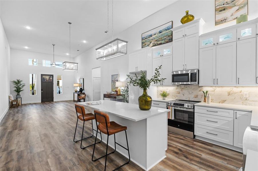 Kitchen featuring dark hardwood / wood-style floors, white cabinetry, a kitchen island, appliances with stainless steel finishes, and decorative light fixtures