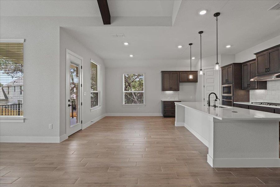Kitchen featuring tasteful backsplash, hanging light fixtures, light wood-type flooring, a kitchen island with sink, and recessed lighting Kitchen featuring tasteful backsplash, hanging light fixtures, light wood-type flooring, a kitchen island with sink, and recessed lighting