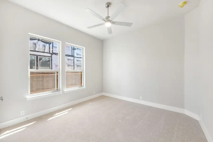 Empty bedroom with carpet flooring, ceiling fan, and two windows in a new construction home