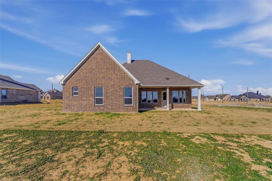 Back of house featuring brick siding, a patio, a yard, and a residential view