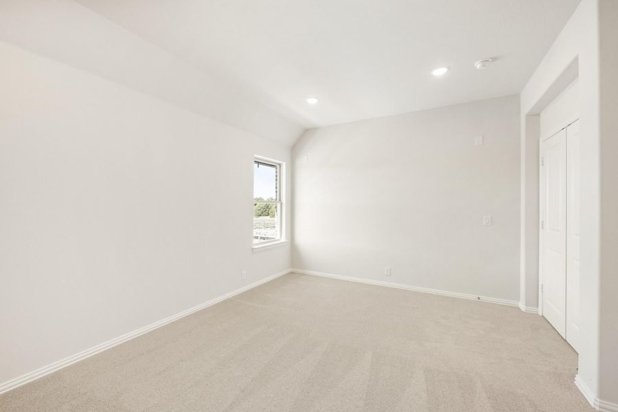 Empty bedroom with beige carpet, white walls, vaulted ceiling, and a closet door Empty bedroom with beige carpet, white walls, vaulted ceiling, and a closet door