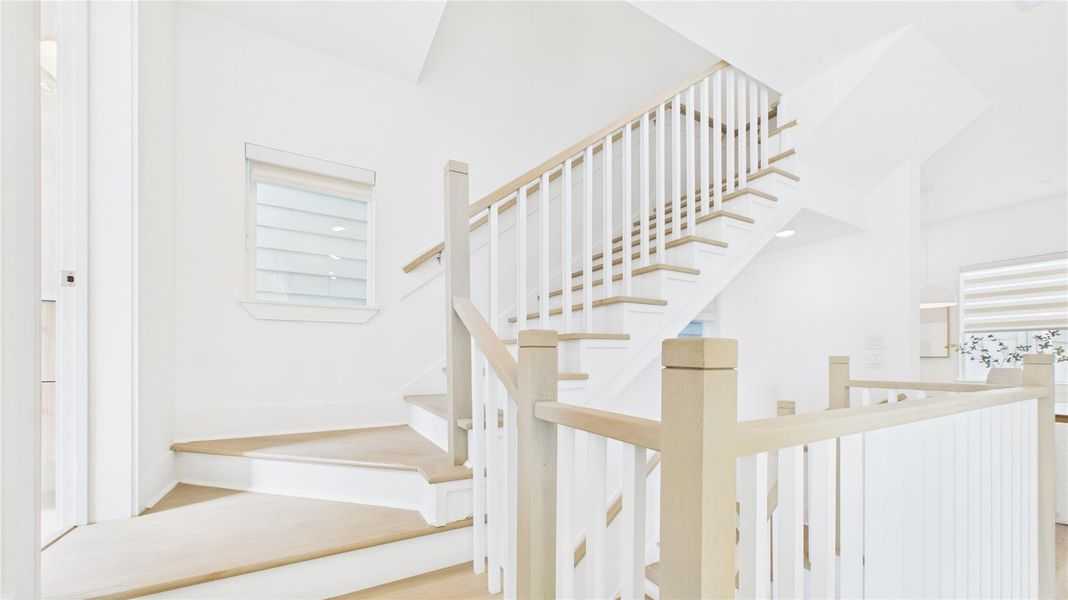 This photo showcases a bright, modern staircase with light wood steps and white railings. The area is well-lit with natural light from a window, creating an airy and inviting atmosphere.