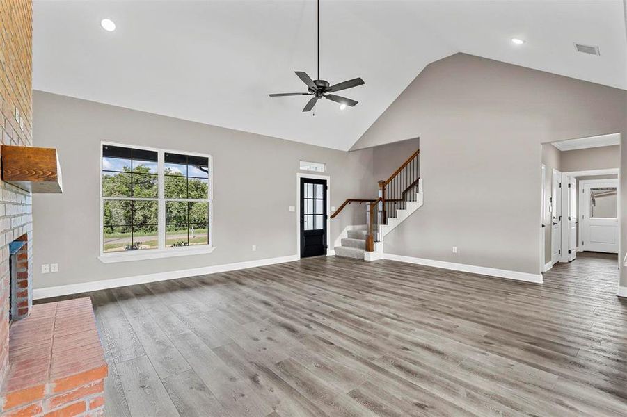 Unfurnished living room featuring ceiling fan, wood-type flooring, high vaulted ceiling, and a fireplace