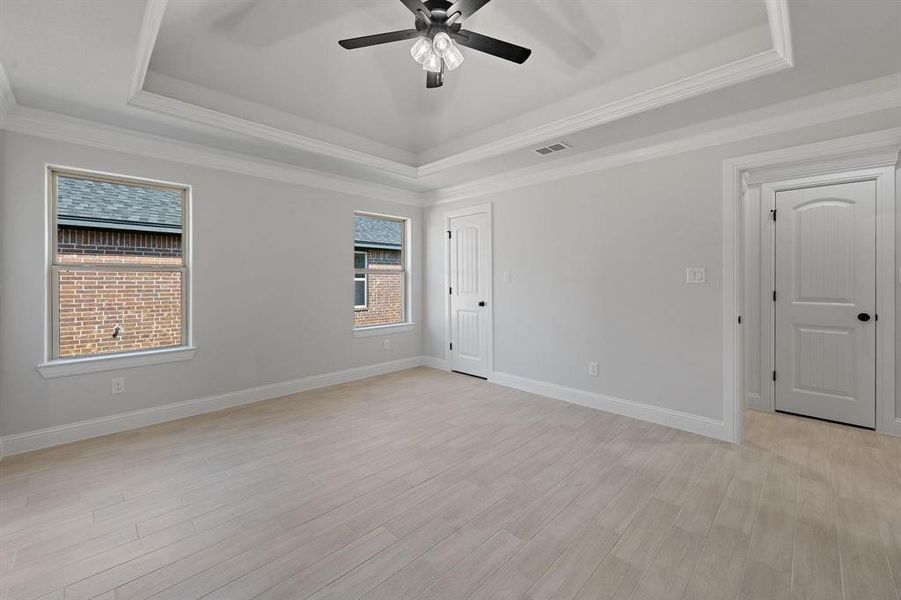 Unfurnished bedroom with light wood finished floors, ceiling fan, crown molding, and a raised ceiling