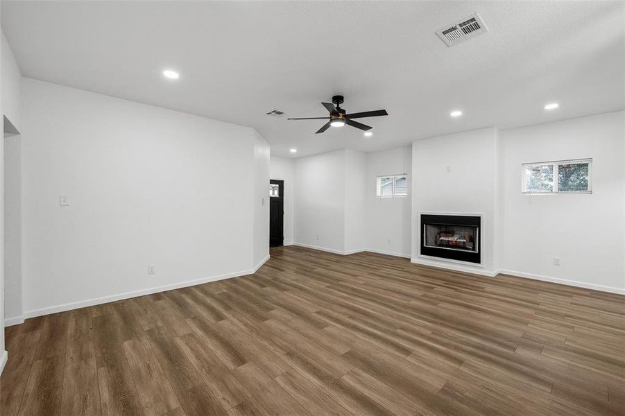 Spacious room featuring wood-finish flooring, a built-in fireplace with a white mantel, two windows, recessed lighting, and a ceiling fan Spacious room featuring wood-finish flooring, a built-in fireplace with a white mantel, two windows, recessed lighting, and a ceiling fan