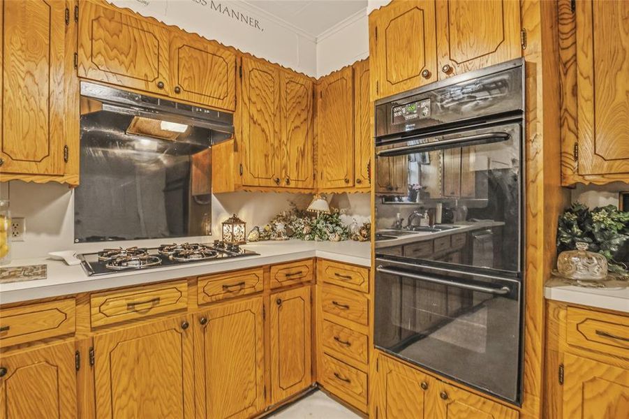 Kitchen featuring wood cabinetry, white countertops, built-in double ovens, and a gas cooktop with an integrated range hood Kitchen featuring wood cabinetry, white countertops, built-in double ovens, and a gas cooktop with an integrated range hood