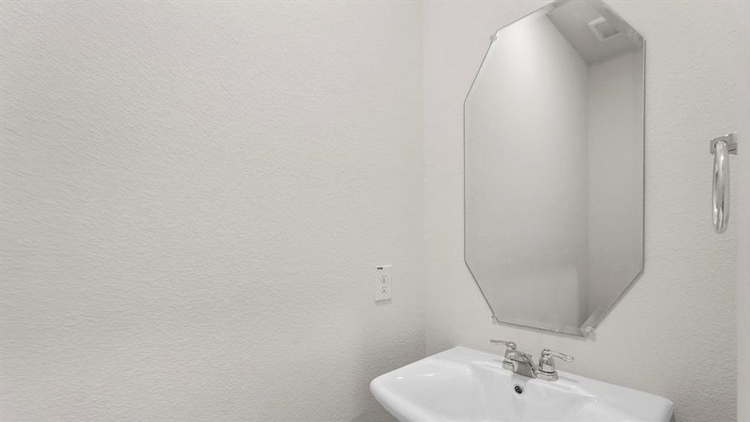 This bathroom features a white pedestal sink with a chrome faucet, a unique octagonal mirror, and a chrome towel ring