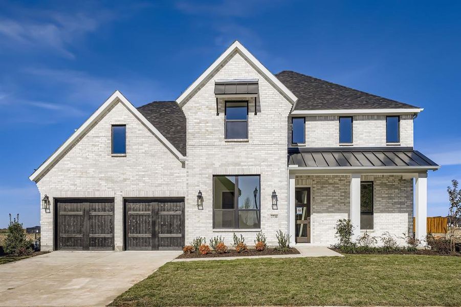 View of front of home with brick siding, a front lawn, a standing seam roof, driveway, and a metal roof