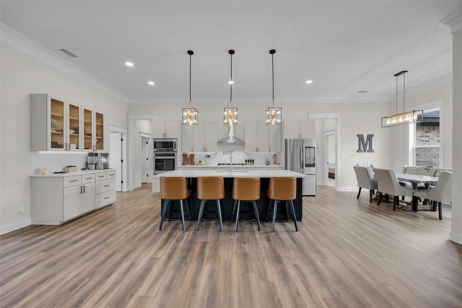 Kitchen featuring white cabinetry, hanging light fixtures, backsplash, a spacious island, and appliances with stainless steel finishes