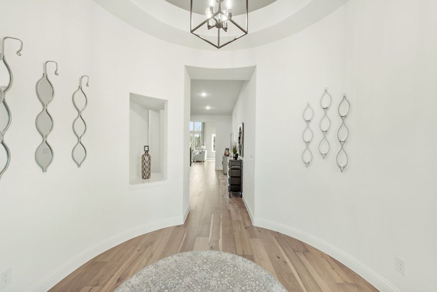 Curved entryway with hardwood floors, tray ceiling, pendant light, and decorative wall art leading to hallway Curved entryway with hardwood floors, tray ceiling, pendant light, and decorative wall art leading to hallway