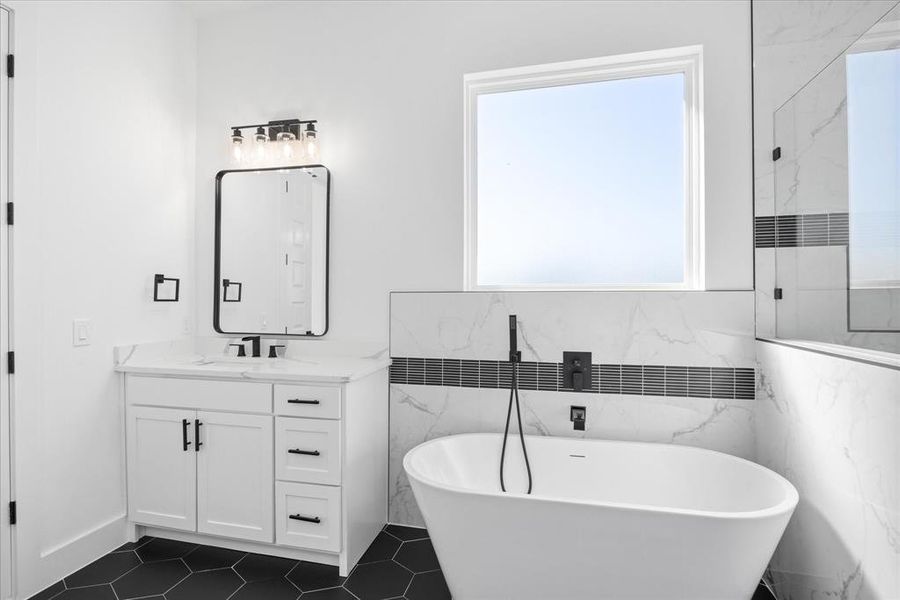 Freestanding soaking tub with matte black fixtures, set against a tiled wall featuring a decorative horizontal accent band