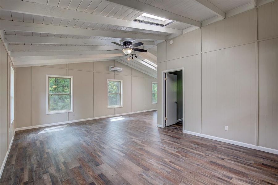 Unfurnished room featuring an AC wall unit, vaulted ceiling with skylight, hardwood / wood-style flooring, wood ceiling, and ceiling fan