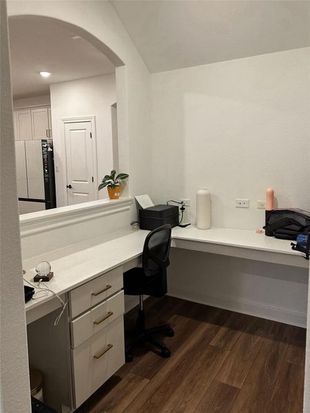 Built-in desk cabinetry featuring three drawers with gold-tone hardware, a white countertop, and wood-finish flooring Built-in desk cabinetry featuring three drawers with gold-tone hardware, a white countertop, and wood-finish flooring