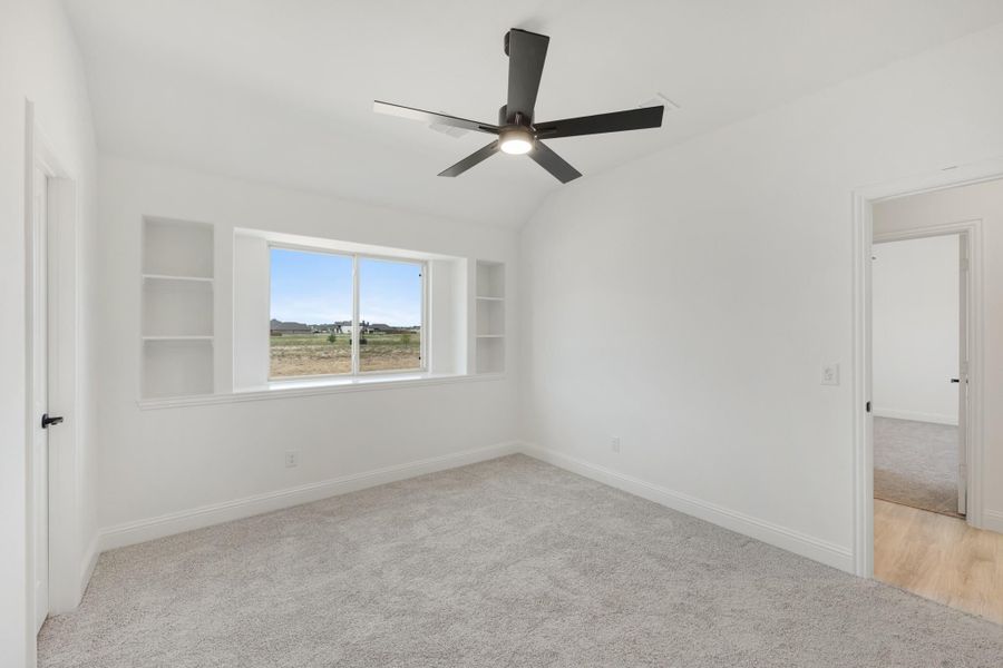 Empty bedroom with vaulted ceiling, black ceiling fan, built-in shelves, and carpet flooring