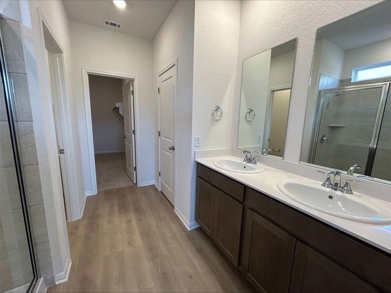 Bathroom featuring a shower stall, double vanity, wood finished floors, and a textured wall Bathroom featuring a shower stall, double vanity, wood finished floors, and a textured wall