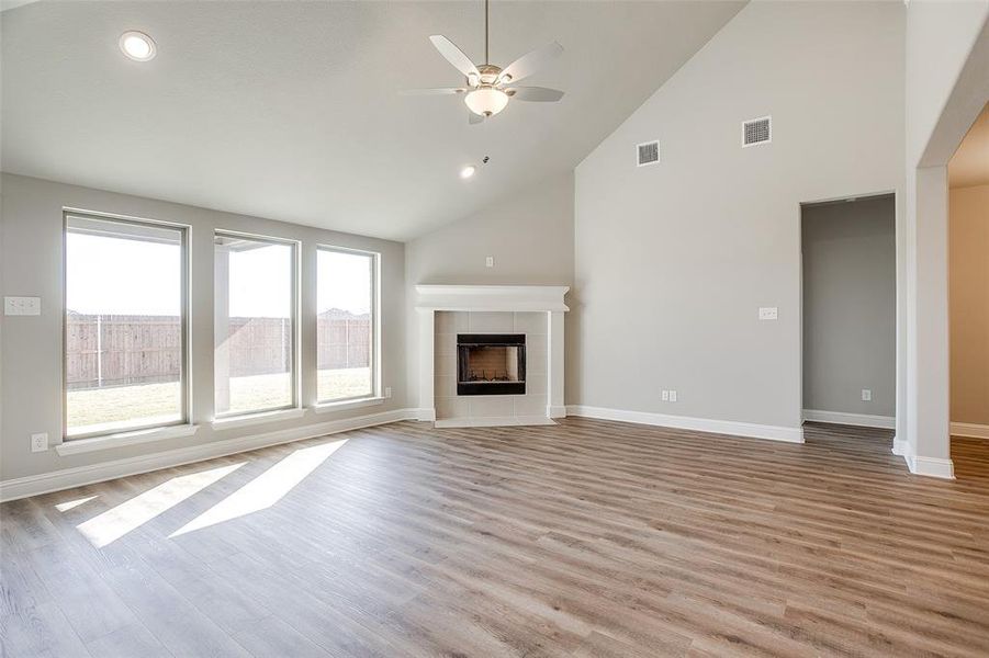 Unfurnished living room featuring a tiled fireplace, ceiling fan, light wood-type flooring, and high vaulted ceiling Unfurnished living room featuring a tiled fireplace, ceiling fan, light wood-type flooring, and high vaulted ceiling