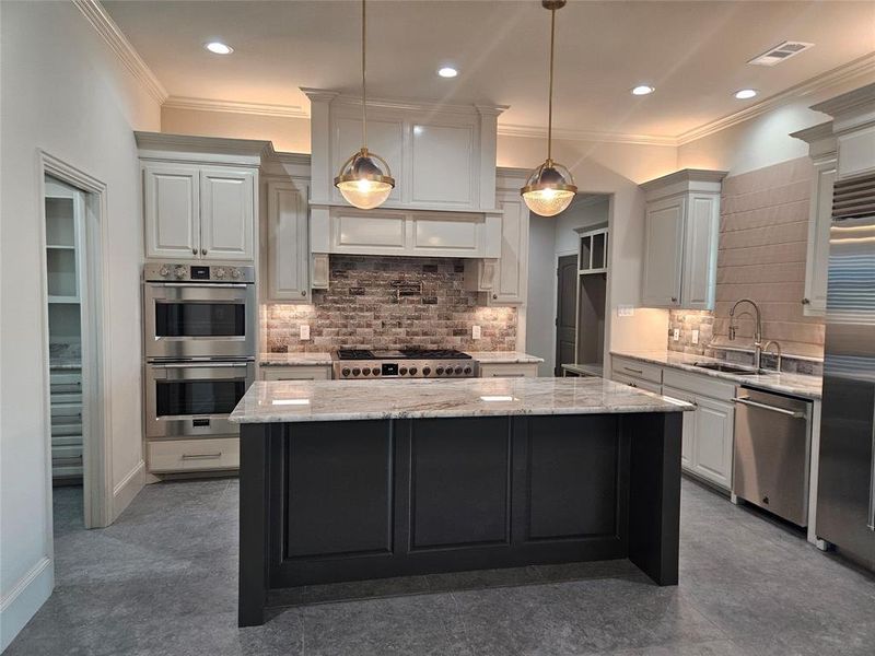 Kitchen with a center island, appliances with stainless steel finishes, light stone counters, and decorative light fixtures