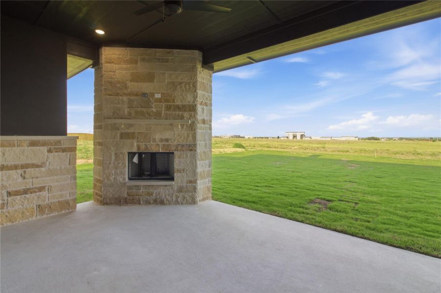 An inviting covered patio featuring a stone fireplace and views of an expansive green field. An inviting covered patio featuring a stone fireplace and views of an expansive green field.