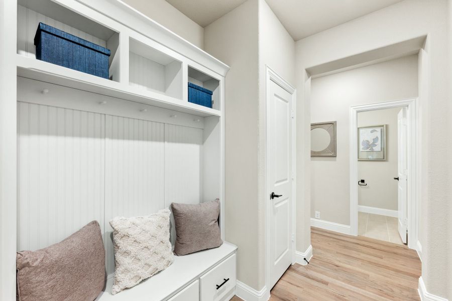 Mudroom with white built-in bench, upper storage cubbies, and light hardwood floors leading to a hallway Mudroom with white built-in bench, upper storage cubbies, and light hardwood floors leading to a hallway