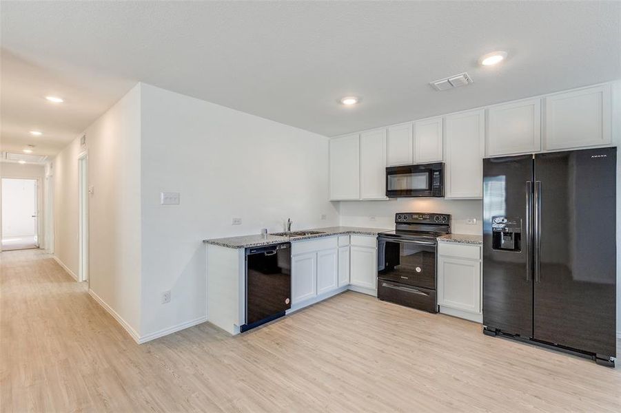 Kitchen with light stone counters, sink, black appliances, light hardwood / wood-style floors, and white cabinetry