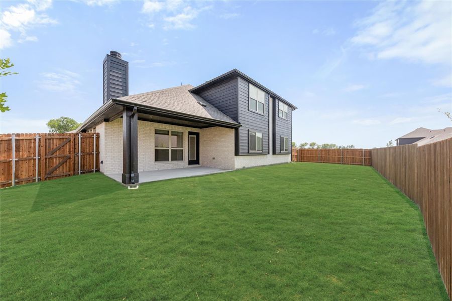 Two-story home rear view with covered patio, large fenced backyard, and dark gray siding over brick exterior.